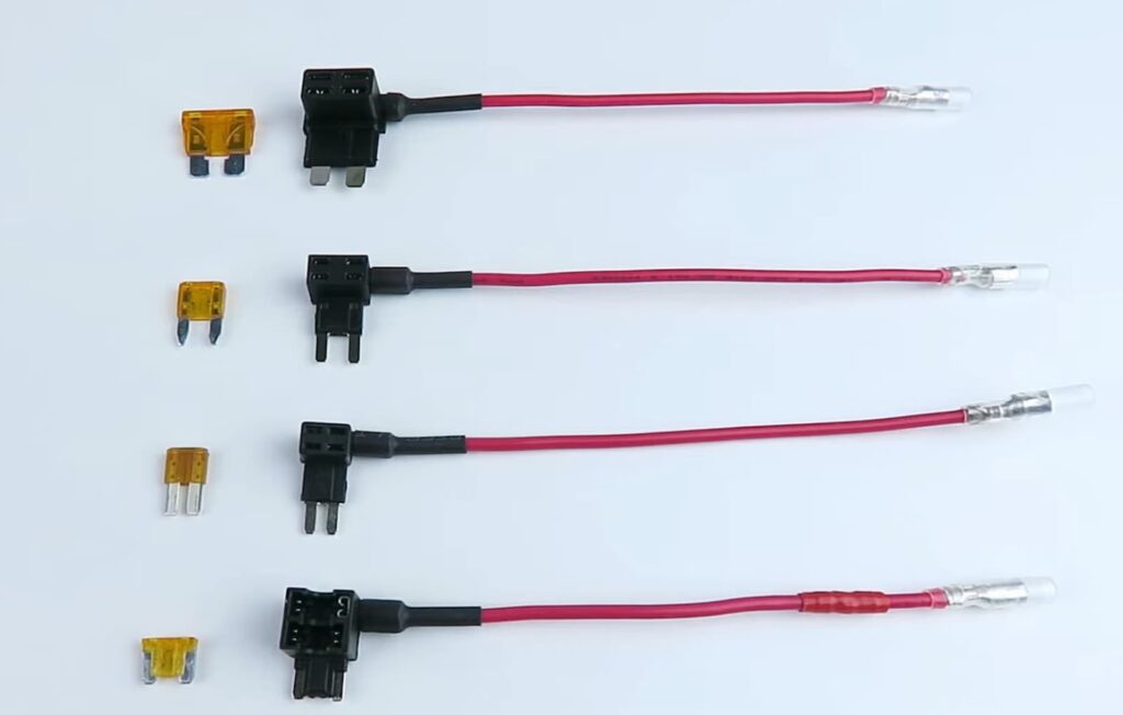 Three fuse taps with red wires attached, accompanied by three corresponding yellow blade fuses, displayed on a white background