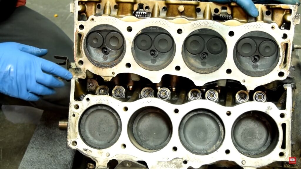 engine block with six cylindrical chambers at the bottom, and gloved hand points to one of the components.